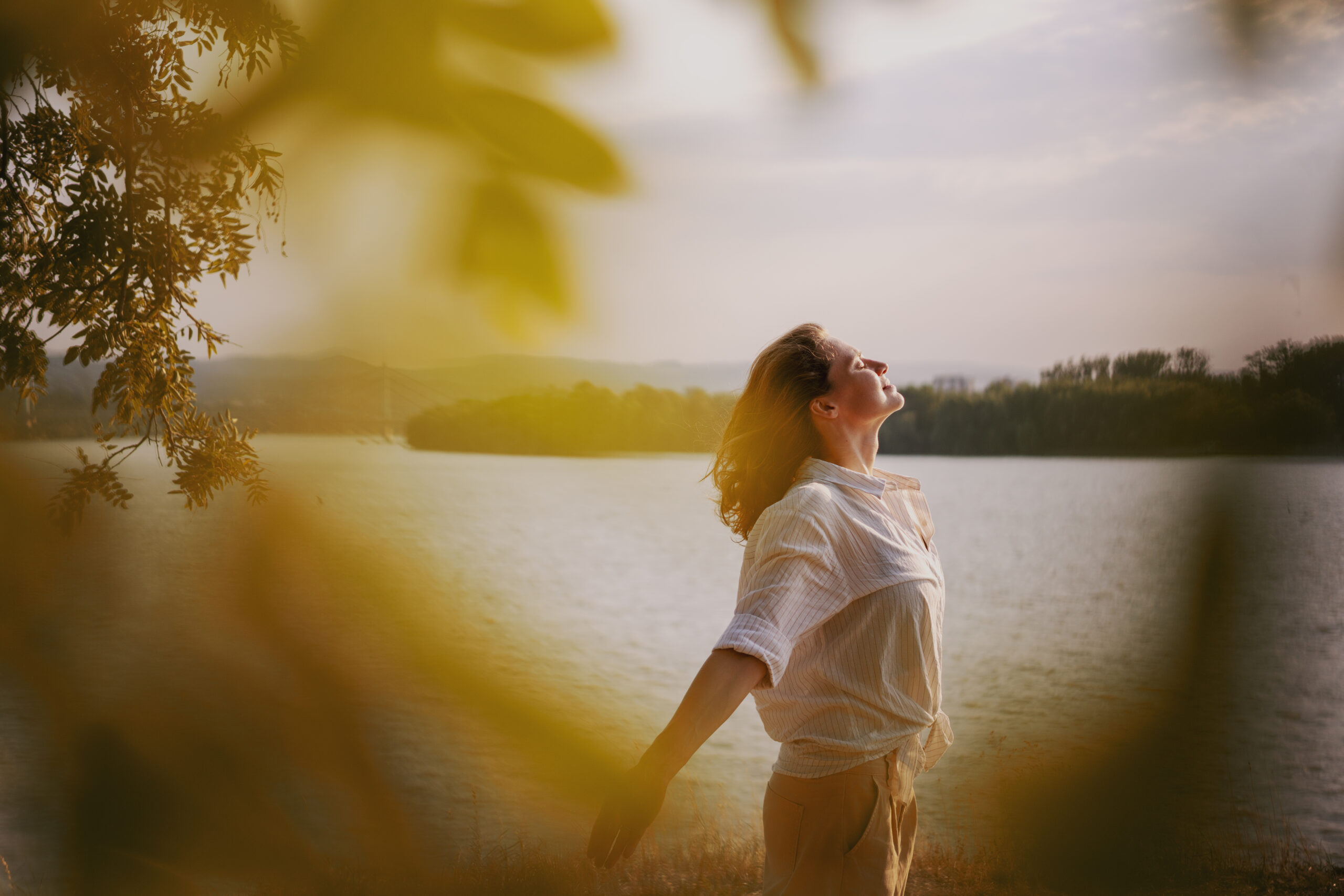 Beautiful young relaxed woman in white blouse enjoying nature breathing fresh air meditating on the river on an autumn